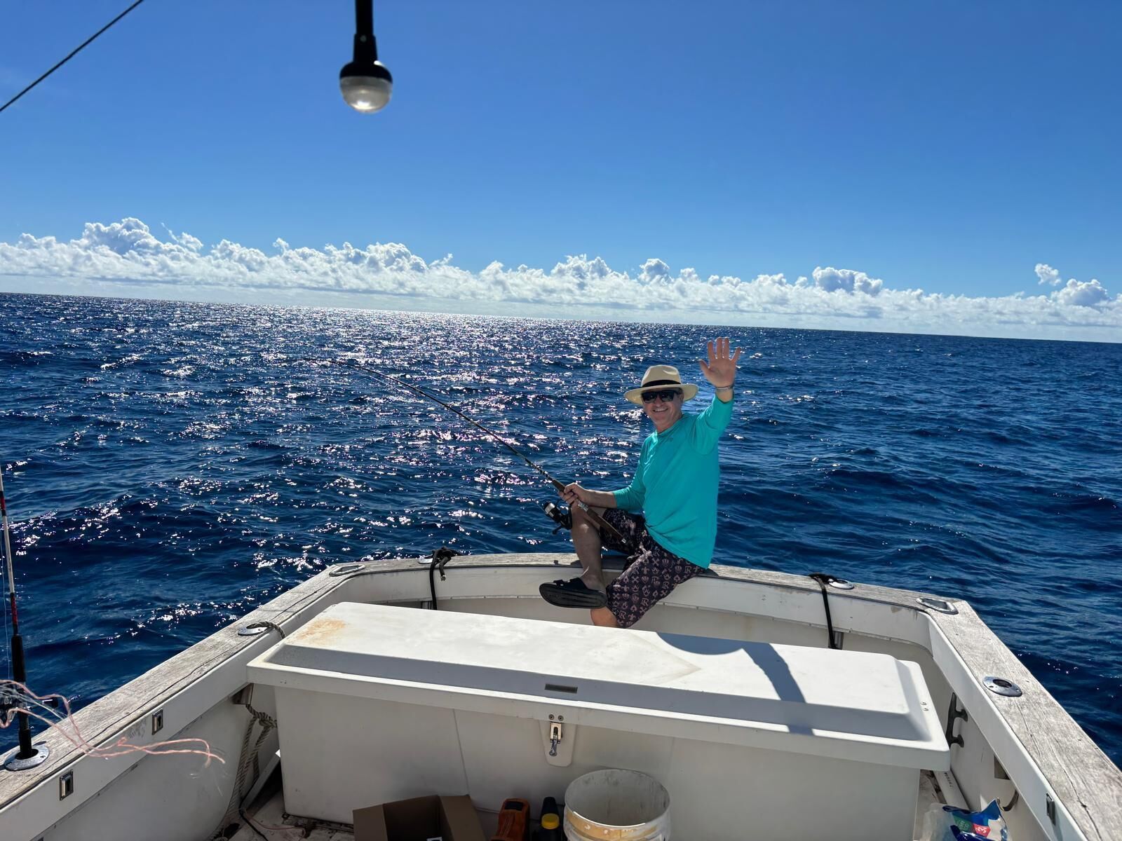 A boat with a person on deck, a fishing rod, and a clear view of the ocean.
