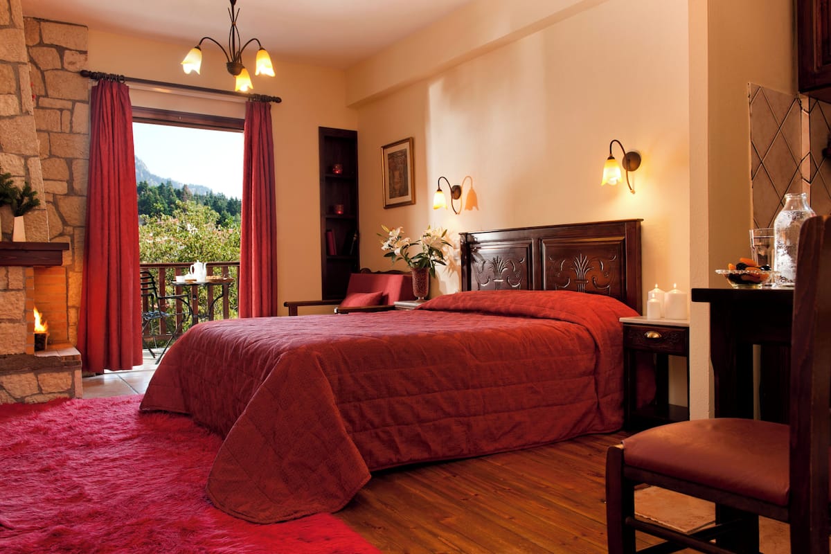 Ein Schlafzimmer mit einem großen Bett, einem Kamin, einem Balkon mit Aussicht und einem Nachttisch mit Kerzen.
