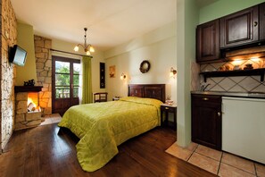 Una habitación con cama, chimenea, zona de cocina y televisor montado en una pared de piedra.