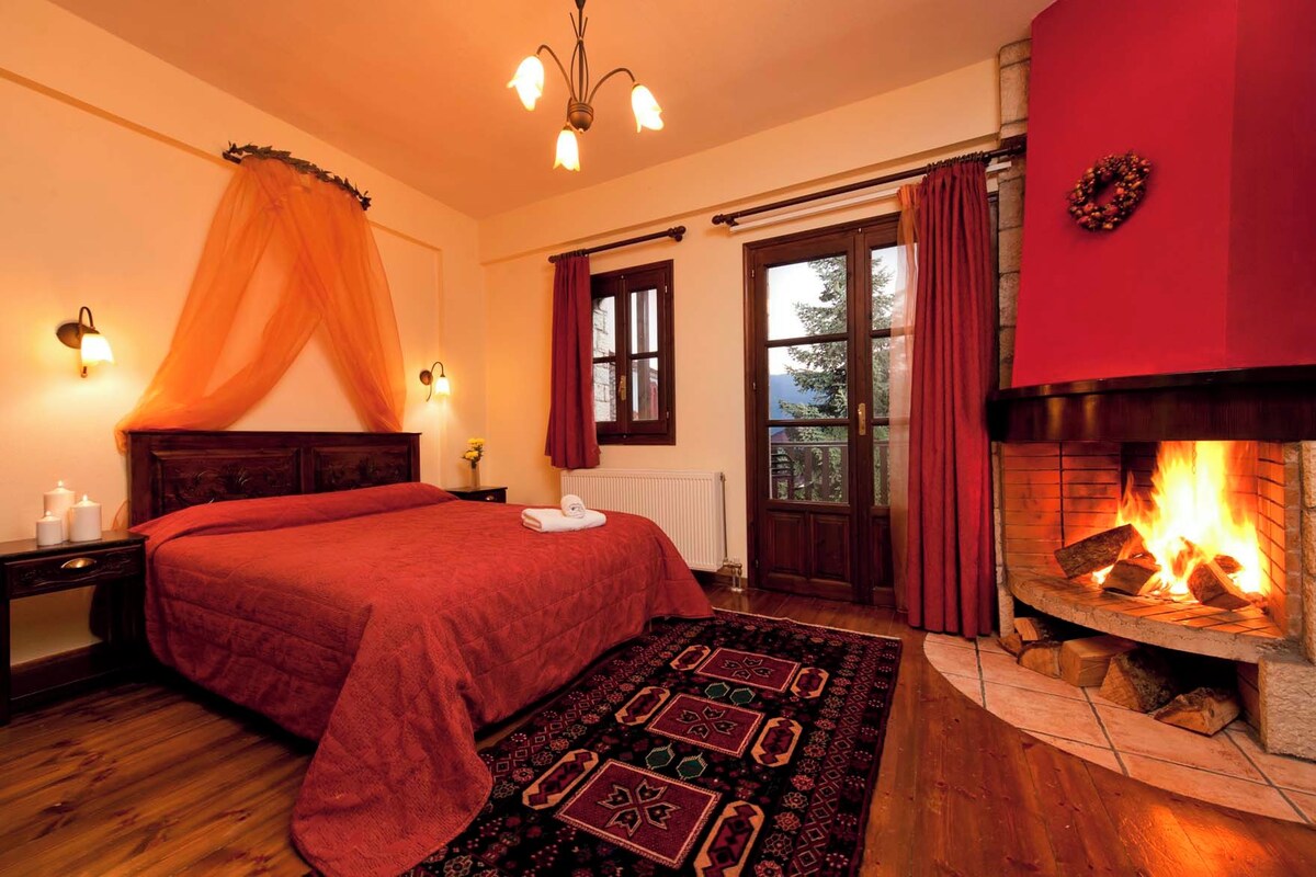 A cozy bedroom with a large bed, a fireplace, and a view of the outdoors.