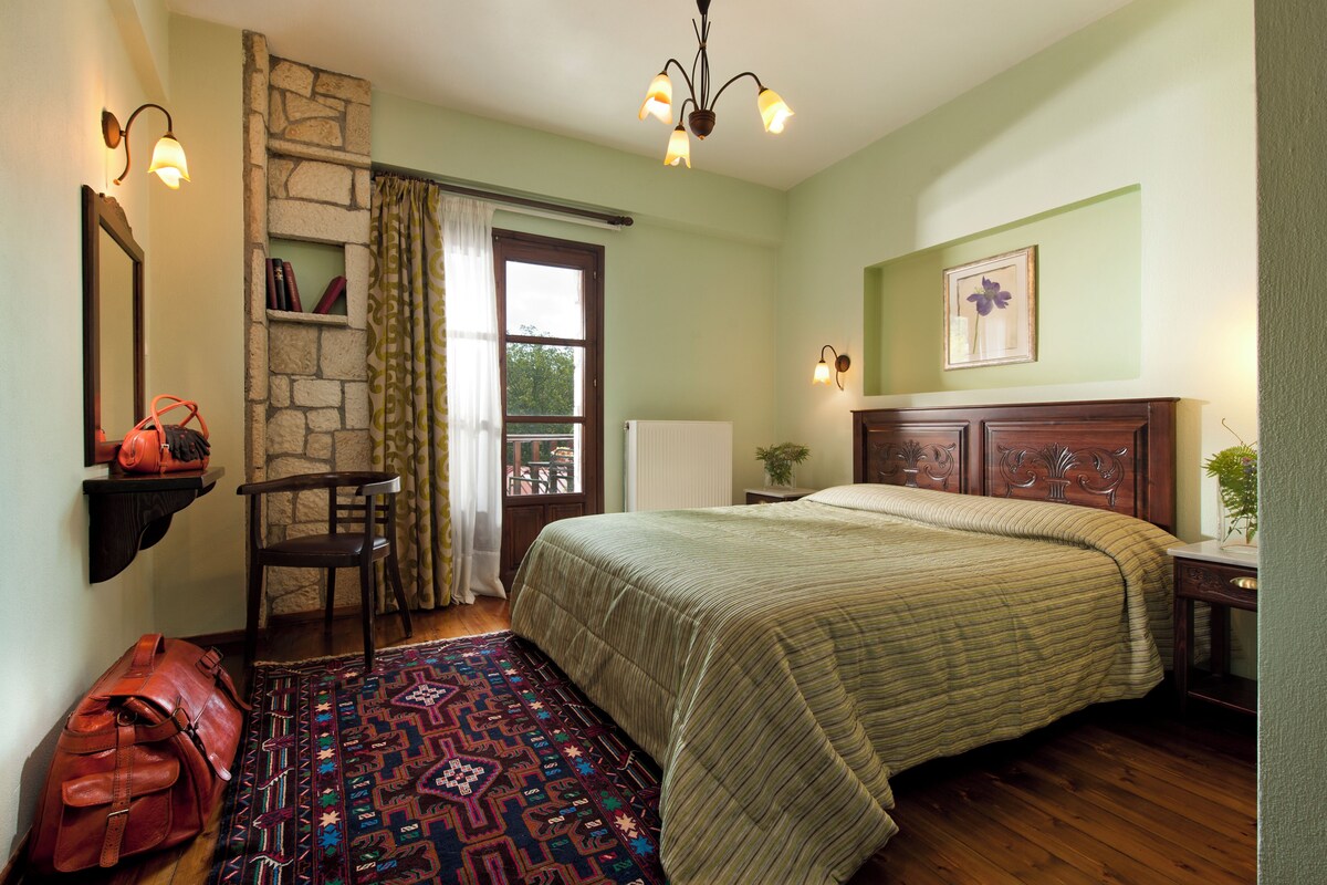 A bedroom with a bed, a chair, a rug, a suitcase, and a stone wall.