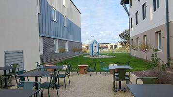 Un área de patio al aire libre con mesas y sillas, un pequeño jardín y un edificio de diseño moderno.