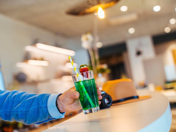 A hand holding a glass with a green drink, a straw, and a garnish. - Ibis Budget Le Treport Mers les Bains (Mers-les-Bains)