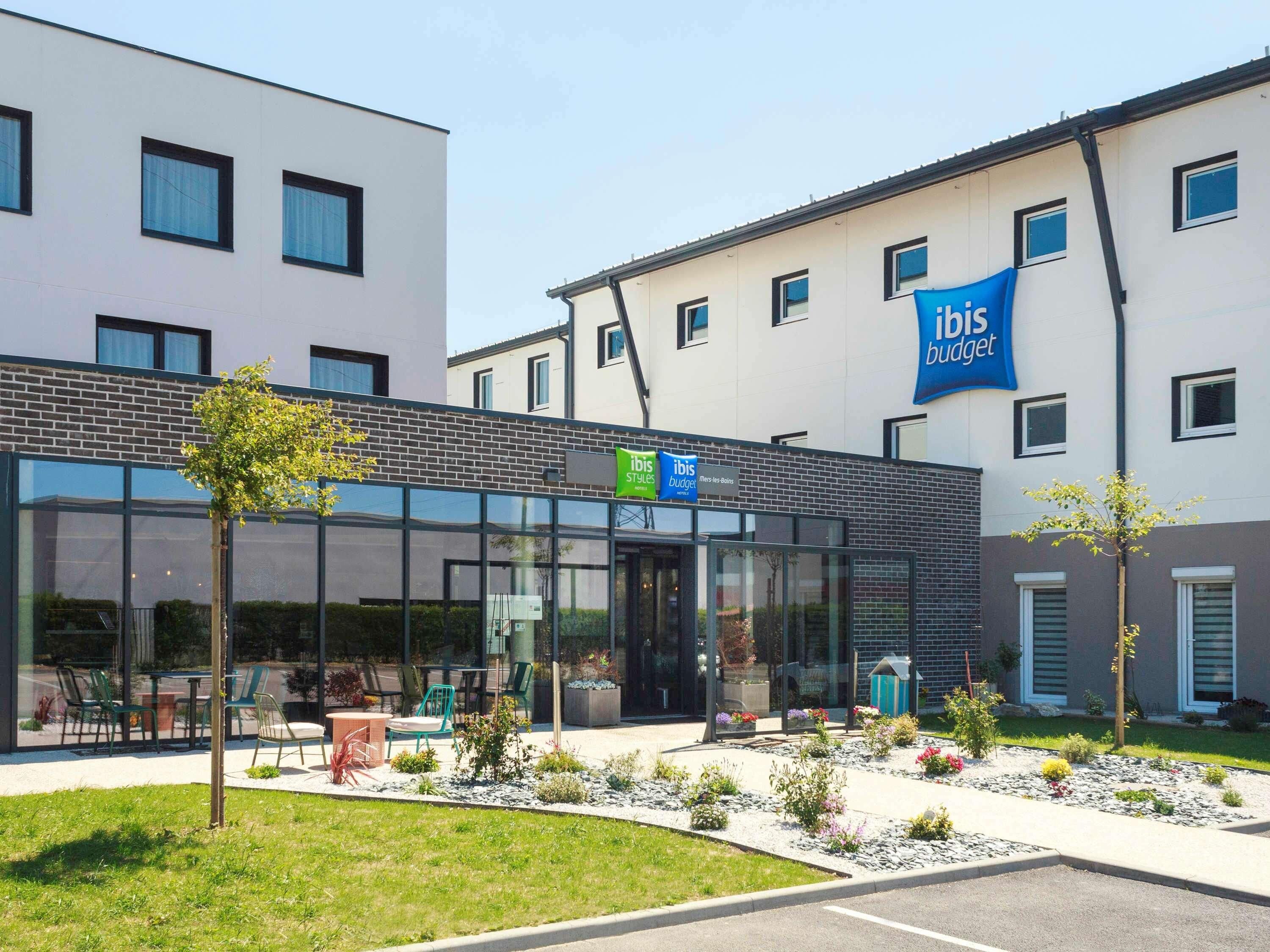 A modern building with a glass facade, outdoor seating area, and a sign for ibis Styles budget hotel.