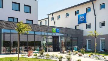 A modern building with a glass facade, outdoor seating area, and a sign for ibis Styles budget hotel.
