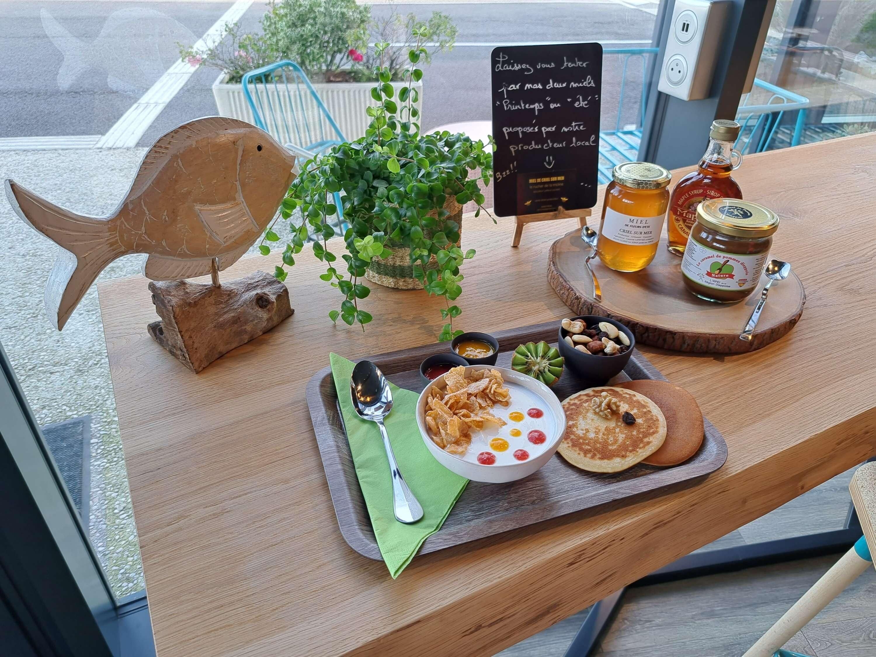 A wooden table with a fish decoration, a potted plant, a sign, jars of honey, and a plate with food.