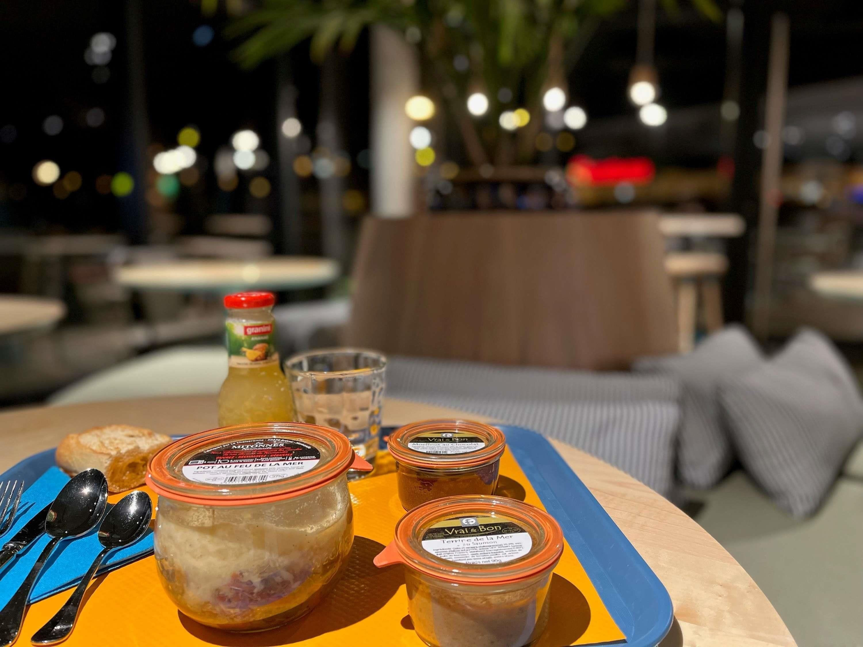 Una mesa con una bandeja que contiene frascos de comida, un vaso de agua y una botella de jugo.