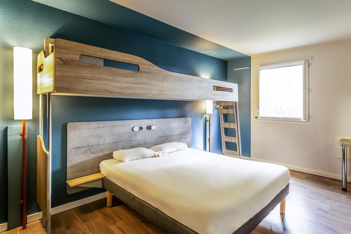 Un dormitorio moderno con una cama litera, una mesita de noche, una lámpara y una ventana.