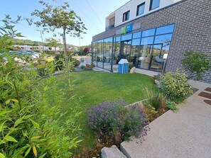 A modern building with a glass facade, a well-maintained lawn, and a small blue structure. - Ibis Budget Le Treport Mers les Bains (Mers-les-Bains)