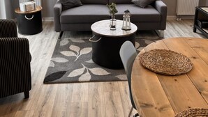 Uma sala de estar moderna com um sofá cinzento, uma mesa de centro redonda e uma mesa de jantar com cadeiras.
