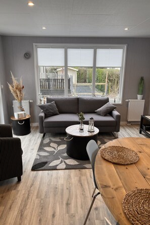 Ein modernes Wohnzimmer mit einem grauen Sofa, einem runden Couchtisch und einem Esstisch mit Stühlen.