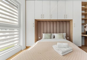 Ein Schlafzimmer mit Bett, Fenster mit Jalousien, einem Schrank mit Holz-Kopfteil und einem Regal mit Dekoration.