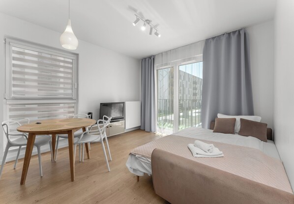 Ein modernes Hotelzimmer mit Bett, Schreibtisch, Stuhl, Fernseher und einem Balkon.