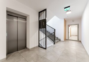 Ein moderner Aufzug, eine Treppe mit Metallgeländer und ein Flur, der in einen anderen Raum führt.