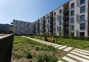 Ein modernes Mehrfamilienhaus mit Balkonen, einem grünen Rasen und einem gepflasterten Weg.