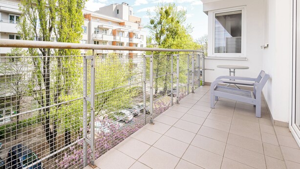 Een balkon met een metalen hekwerk, een tafeltje en een bank.