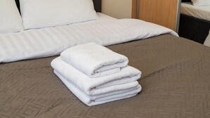 Een net opgemaakt bed met een opgevouwen witte handdoek, een bedsprei met bruin patroon en een houten hoofdeinde.