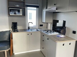 A compact kitchen with a gas stove, a coffee maker, and a window with blinds. - Vakantiepark Klein Strand - Cottage 6p by Interhome (Jabbeke)