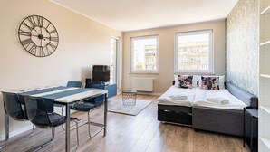 Habitació moderna amb taula de dinar, cadires, un sofà-llit, televisió i finestres grans.