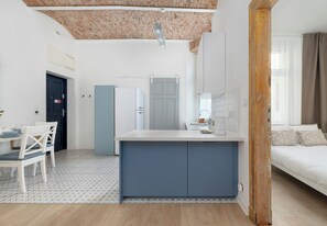 Eine moderne Küche mit einer zentralen Kochinsel, einem Essbereich mit Stühlen, einem weißen Sofa und einer Holzbalkendecke.