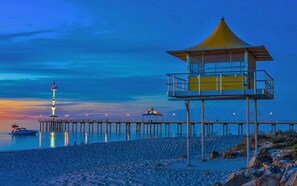 A pier extending into calm waters with a lifeguard tower and a flagpole. - Mantra Adelaide Central (Adelaide)