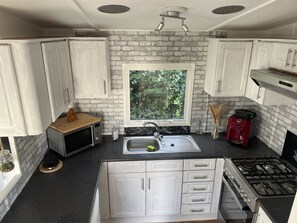 A kitchen with white cabinets, a window, a sink, a microwave, a stove, and a brick wall. - RBR 546 - Beach Resort Kamperland by Interhome (Kamperland)