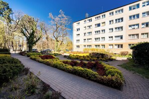 Ein Gebäude mit zahlreichen Fenstern und einem gepflasterten Weg, flankiert von geschnittenen Büschen.