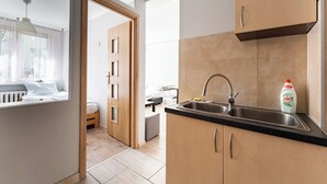 Cocina moderna con un lavamanos, armarios de madera y vista hacia un dormitorio.