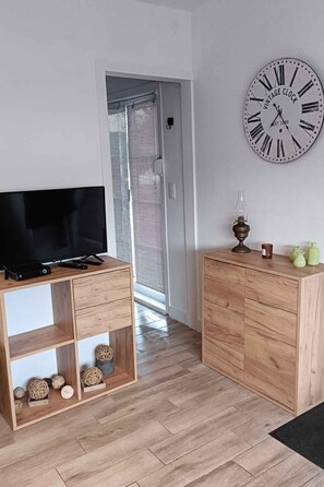 Ein modernes Wohnzimmer mit einem Flachbildfernseher auf einem Holz-TV-Schrank, einer Vintage-Uhr an der Wand und einer Holzkabine mit Schubladen.