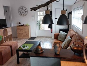 Ein modernes Wohnzimmer mit einer Couch, einem Couchtisch und einem Fernseher. An der Wand hängt eine Uhr und ein Fenster mit Jalousien.