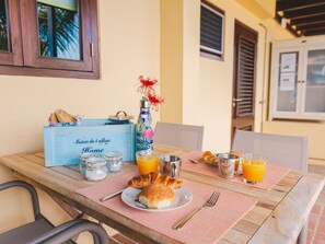 Een ontbijttafel met croissants, sinaasappelsap en een blauwe koffer met de tekst 'Maison du 5 village Home'.