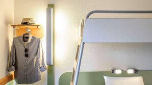 A bunk bed with a pillow, a hanging shirt, and a hat on a shelf. - Ibis Budget Berlin Ost (Berlin)
