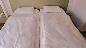 Uma cama de casal com roupa de cama branca, cabeceira verde e mesa de cabeceira com abajur.