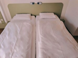 A twin bed with white linens, a green headboard, and a bedside table with a lamp. - Ibis Budget Berlin Ost (Berlin)