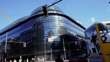A modern building with a curved glass facade, a traffic light, and a bus with 'NEXT EXIT' signage.