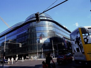 A modern building with a curved glass facade, a traffic light, and a bus with 'NEXT EXIT' signage. - Ibis Budget Berlin Ost (Berlin)
