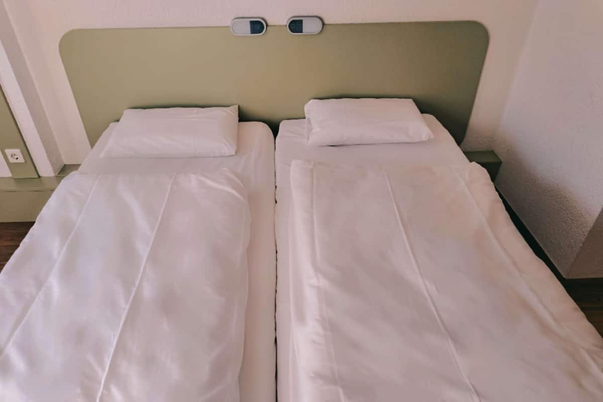 Ein Doppelbett mit weißer Bettwäsche, einem grünen Kopfteil und einem Nachttisch mit Lampe.