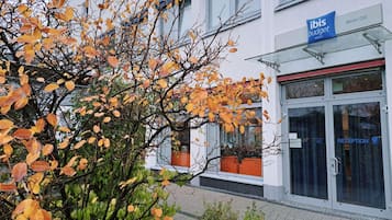 A hotel entrance with a reception desk, a sign for 'ibis budget hotels,' and a building with a white facade.