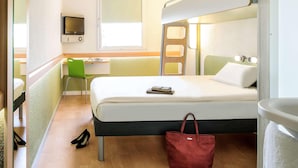 A compact hotel room with a bunk bed, a desk with a chair, a television, and a window. - Ibis Budget Berlin Ost (Berlin)