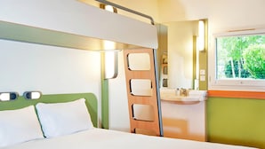 A hotel room with a bed, a bathroom with a sink, and a window with a view of trees. - Ibis Budget Berlin Ost (Berlin)