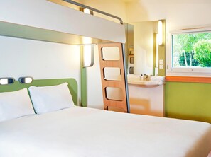 A hotel room with a bed, a bathroom with a sink, and a window with a view of trees. - Ibis Budget Berlin Ost (Berlin)