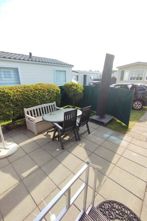 A patio area with a table and chairs, a white bench, and a green fence. - ZP 468 - Camping de Zandput by Interhome (Vrouwenpolder)
