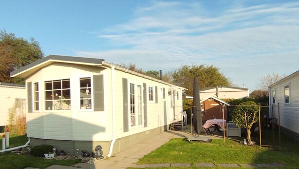 Ein Bungalow mit Veranda, ein kleiner Garten mit Baum und einem wolkenlosen Himmel.