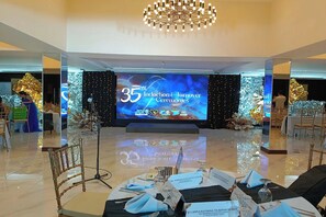 Una sala conferenze con un palco, sedie e un grande schermo che mostra i dettagli dell'evento.