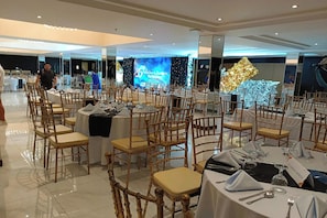 Una sala per banchetti con tavoli rotondi, sedie e un palco con uno sfondo.