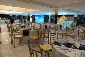 A banquet hall with round tables, chairs, and a stage with a backdrop. - The VIP Hotel by Zuzu (Cagayan de Oro)