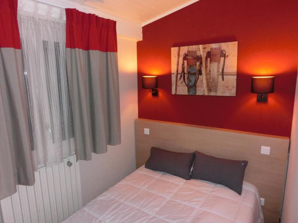 Une chambre d’hôtel avec un lit, des murs rouges, un tableau et deux lampes fixées au mur.