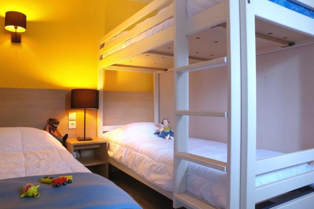 A room with bunk beds, a bedside table with a lamp, and a toy on the bed.