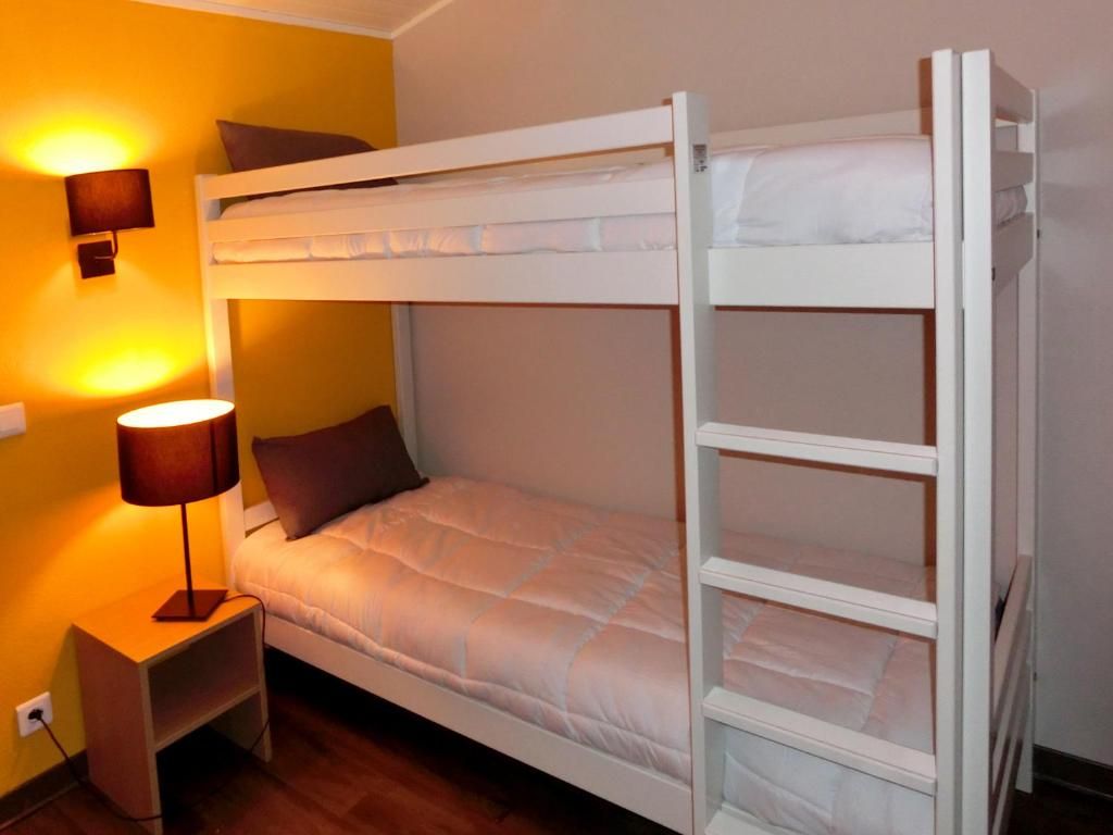 Un lit superposé avec une table de chevet et une lampe, dans une pièce aux murs jaunes et au plancher en bois.