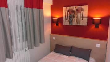 Une chambre d’hôtel avec un lit, des murs rouges, un tableau et deux lampes fixées au mur.
